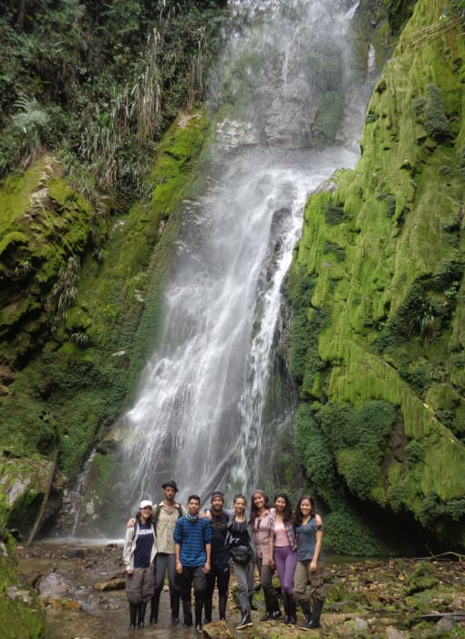 Hiking to the Cascadas Gemelas group of people stands before a waterfall that rushes down a mossy green rock face located in the Intag Valley